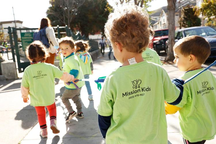 Backs of Children from Mission Kids Preschool walking to Garfield Square Playground on Monday, Nov. 28, 2022.